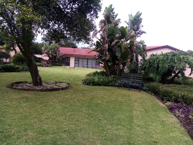 A well-maintained rear garden featuring a lush lawn, mature trees, and established landscaping, providing a private outdoor space adjacent to the home.