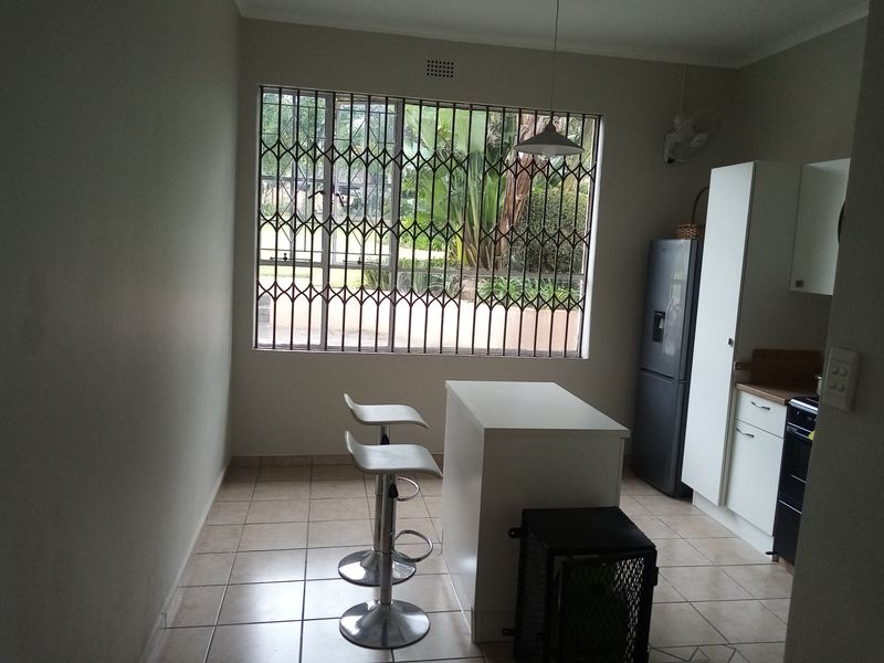A functional kitchen featuring tiled flooring, built-in cabinetry, a central island, and a large window secured with a metal gate.