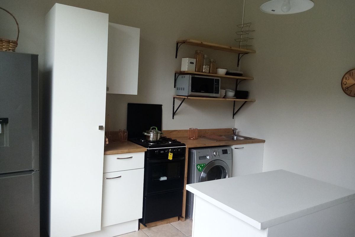 Compact kitchen featuring white cabinetry, wooden countertops, open shelving, a gas stove, and integrated laundry appliance space.