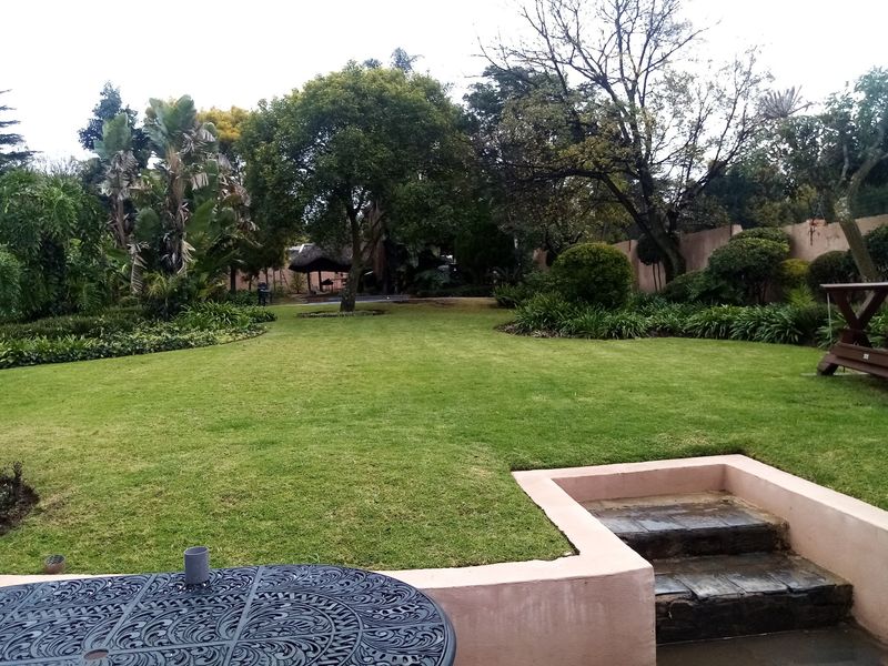 A well-maintained, spacious garden featuring a manicured lawn, mature trees, and a stone-stepped retaining wall leading to the outdoor area.