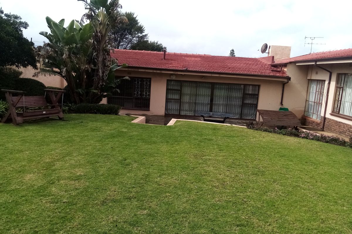 Rear view of the house featuring a well-maintained lawn, tiled roof, and sliding glass doors with security gates.