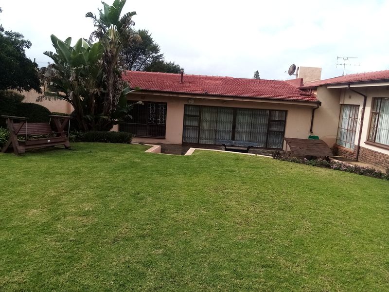 Rear view of the house featuring a well-maintained lawn, tiled roof, and sliding glass doors with security gates.
