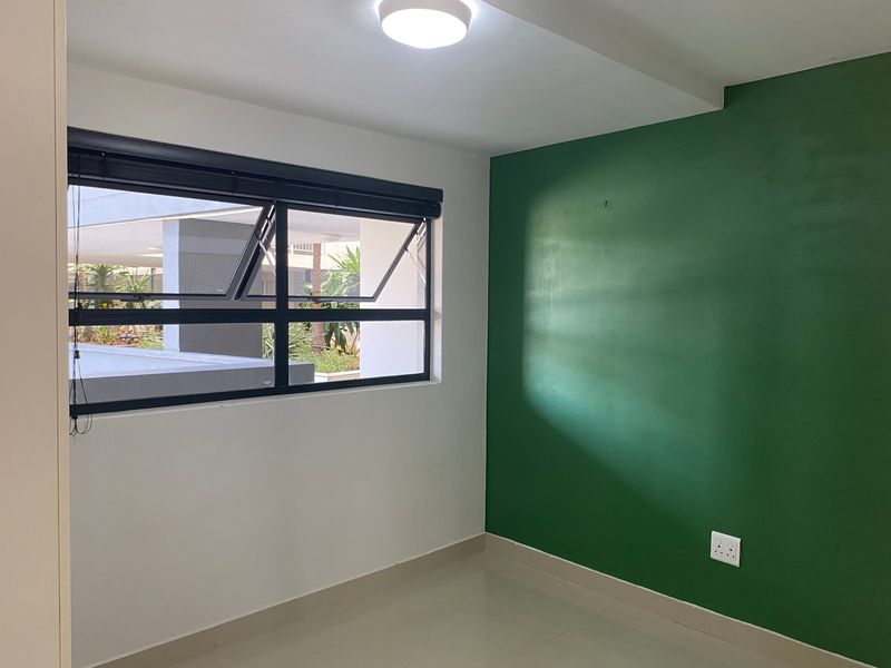 A bright, empty bedroom featuring a green accent wall, tiled flooring, and an awning window with a black frame.