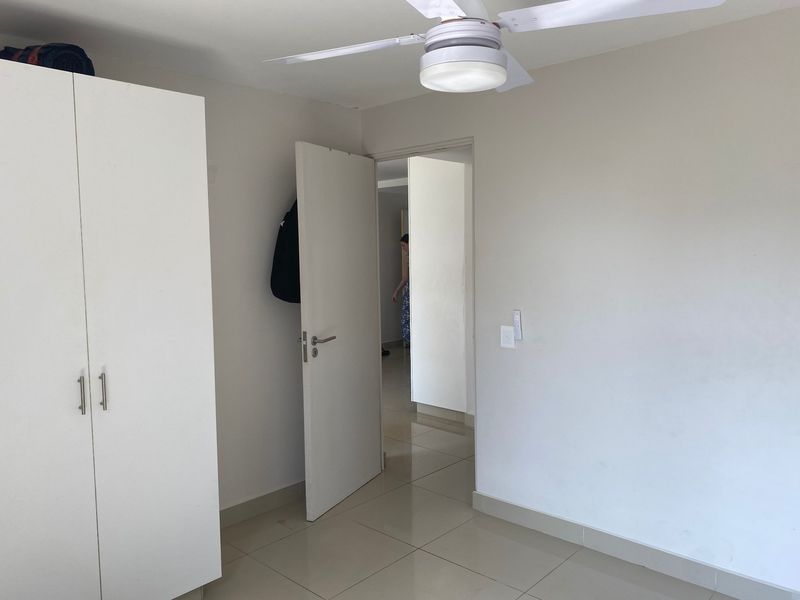 A clean, neutral bedroom featuring tiled flooring, a built-in wardrobe, and a ceiling fan, offering a bright and functional living space.