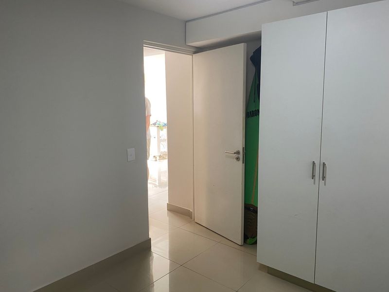 A clean, minimalist bedroom featuring neutral tiled flooring and a white built-in wardrobe, offering a bright and functional living space.