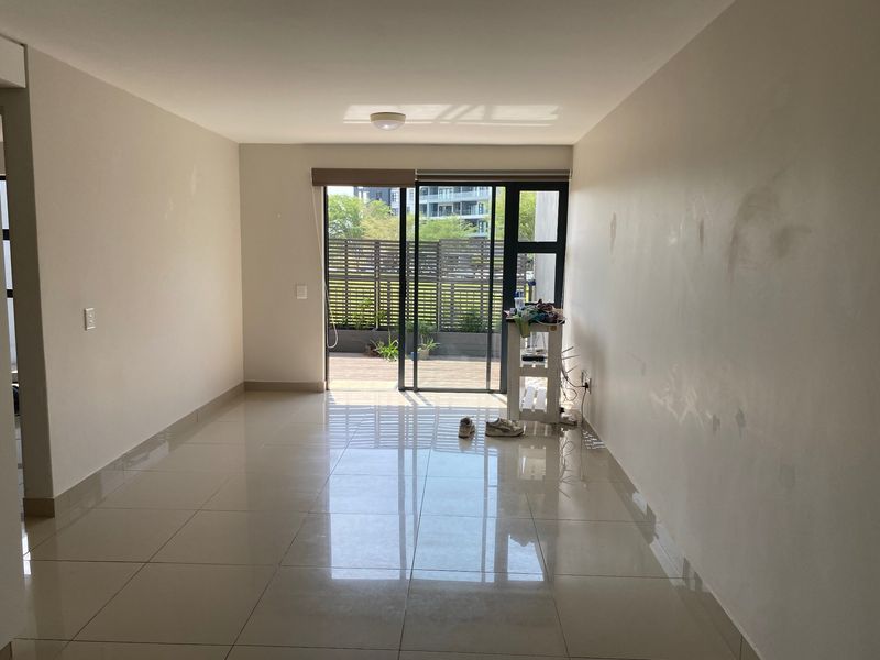 An empty living room featuring large format floor tiles and a sliding glass door leading to an outdoor patio area.