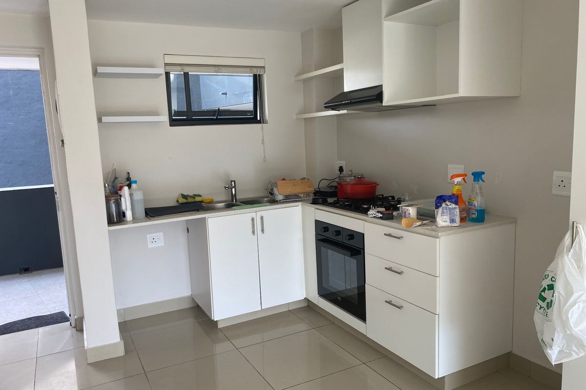 A compact, modern kitchen featuring white cabinetry, a gas hob, built-in oven, extractor fan, and tiled flooring with direct access to an outdoor area.