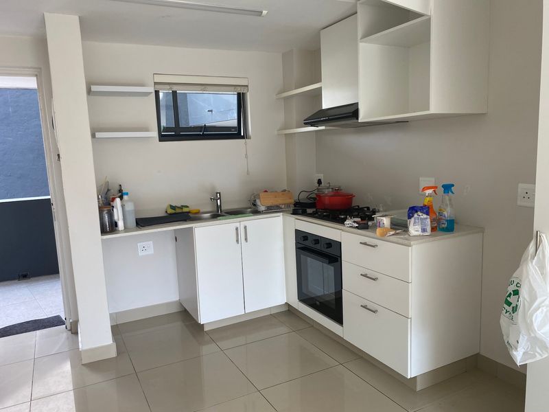 A compact, modern kitchen featuring white cabinetry, a gas hob, built-in oven, extractor fan, and tiled flooring with direct access to an outdoor area.