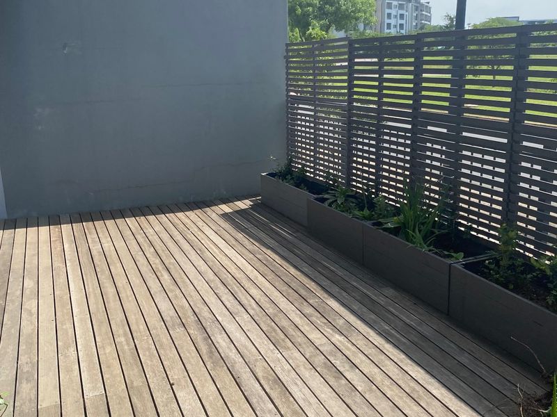 A private outdoor balcony featuring timber decking, a slatted privacy screen, and integrated planter boxes, offering a clean space for outdoor relaxation.