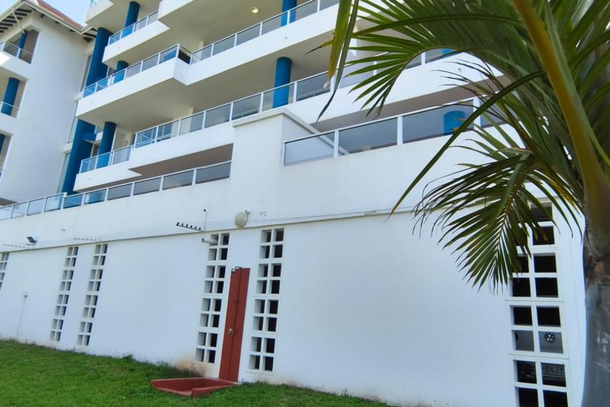 Rear elevation of a multi-story apartment building featuring tiered balconies with glass balustrades, an outdoor shower, and decorative breeze block wall detailing.