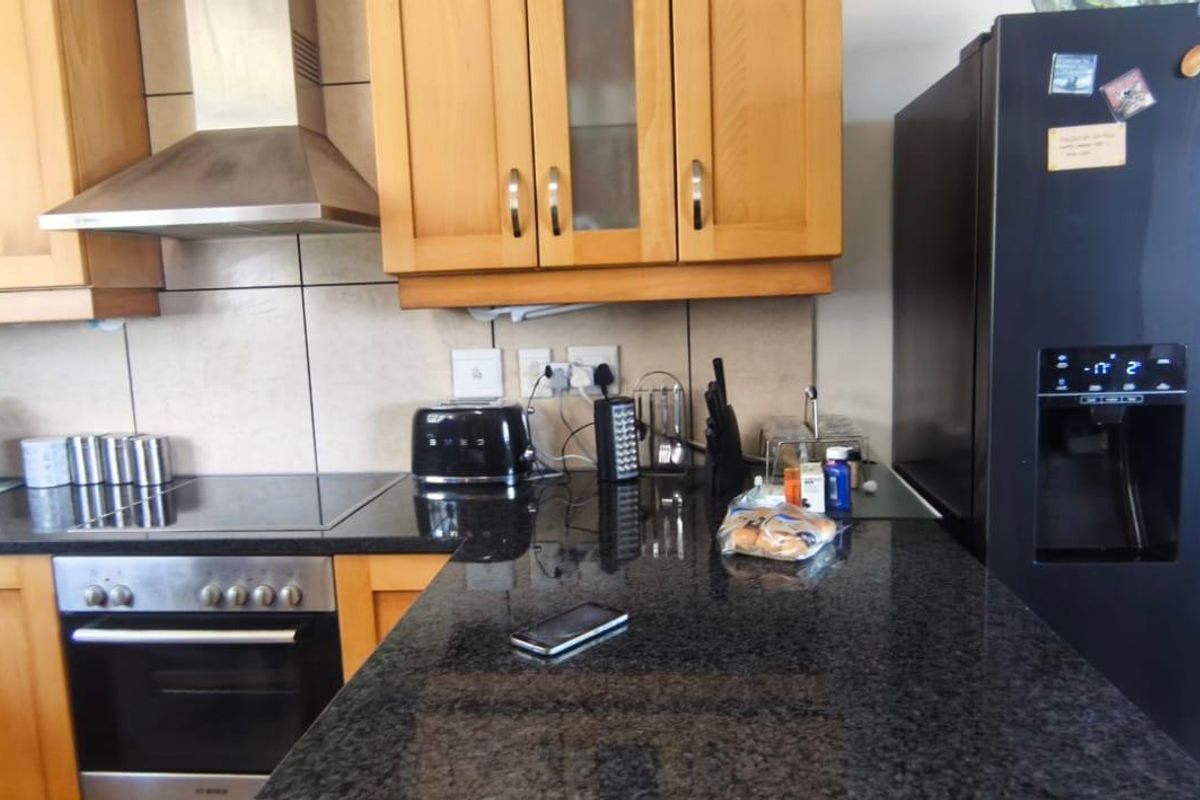 A functional kitchen featuring wooden cabinetry, granite countertops, a tiled backsplash, and integrated stainless steel appliances including an oven and extractor fan.