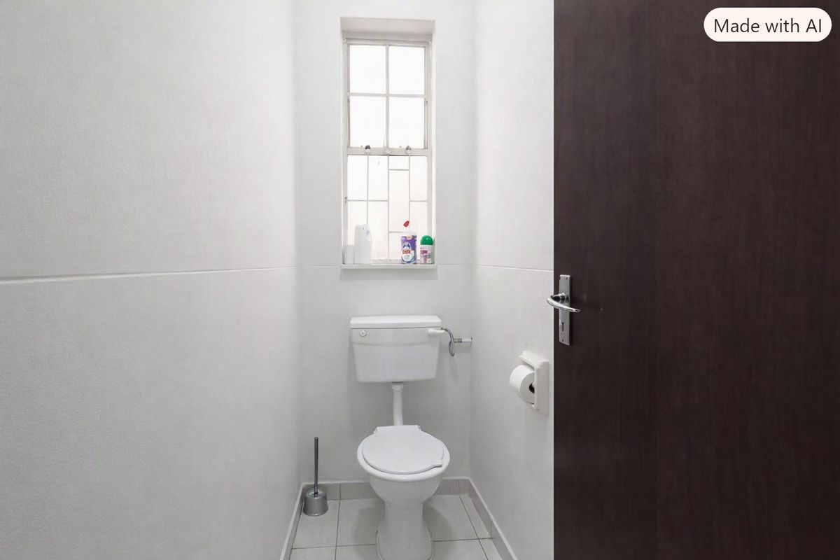 A compact, functional guest bathroom featuring tiled flooring, a standard toilet, and a window with security bars.