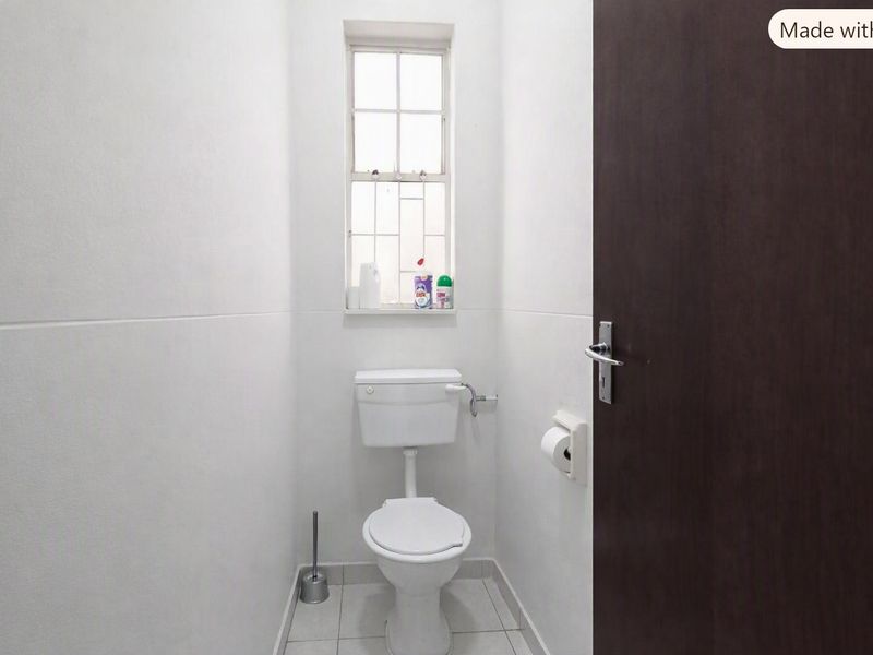 A compact, functional guest bathroom featuring tiled flooring, a standard toilet, and a window with security bars.