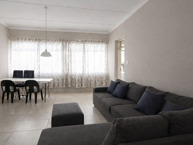 An open-plan living and dining area featuring neutral tiled flooring, coved ceilings, and large windows allowing for ample natural light.