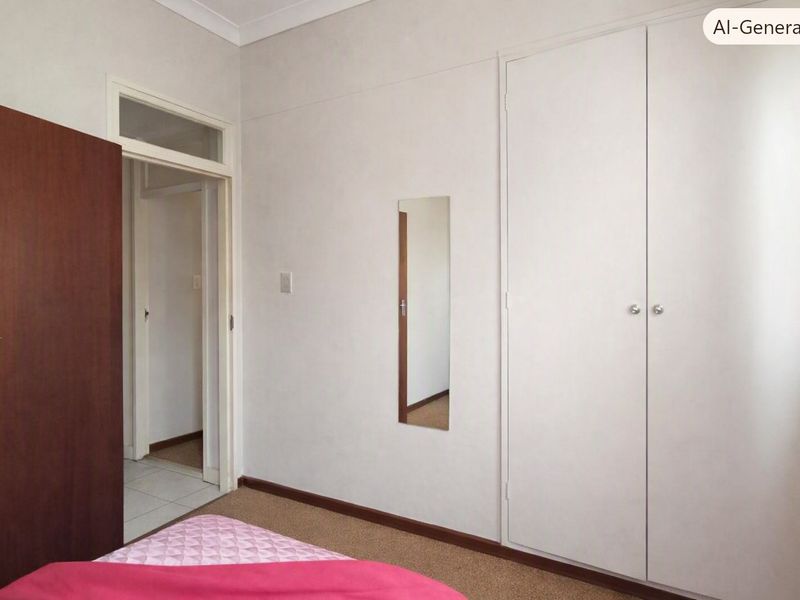 A bedroom featuring neutral walls, carpeted flooring, and a built-in wardrobe with white doors, providing a clean and functional living space.