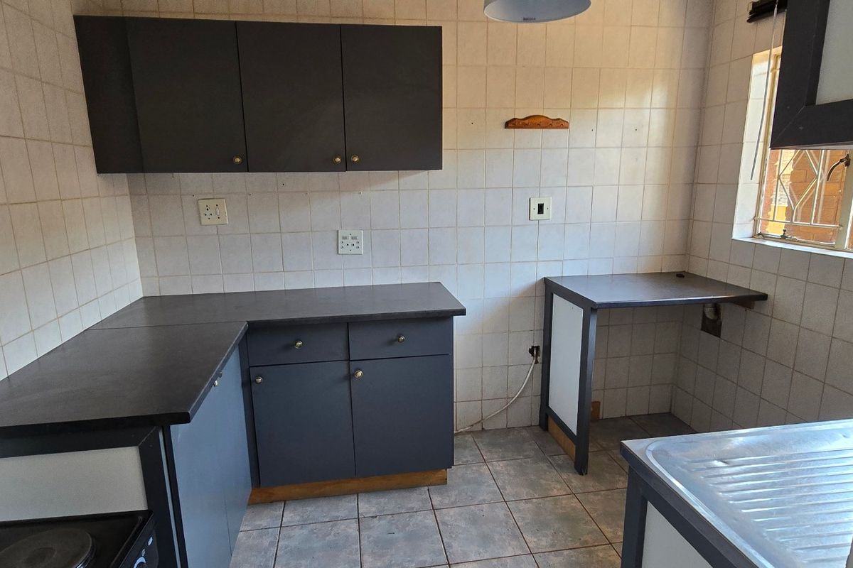 A functional, empty kitchen featuring dark cabinetry, tiled backsplash, and tiled flooring, offering a blank canvas for modern renovation and design updates.