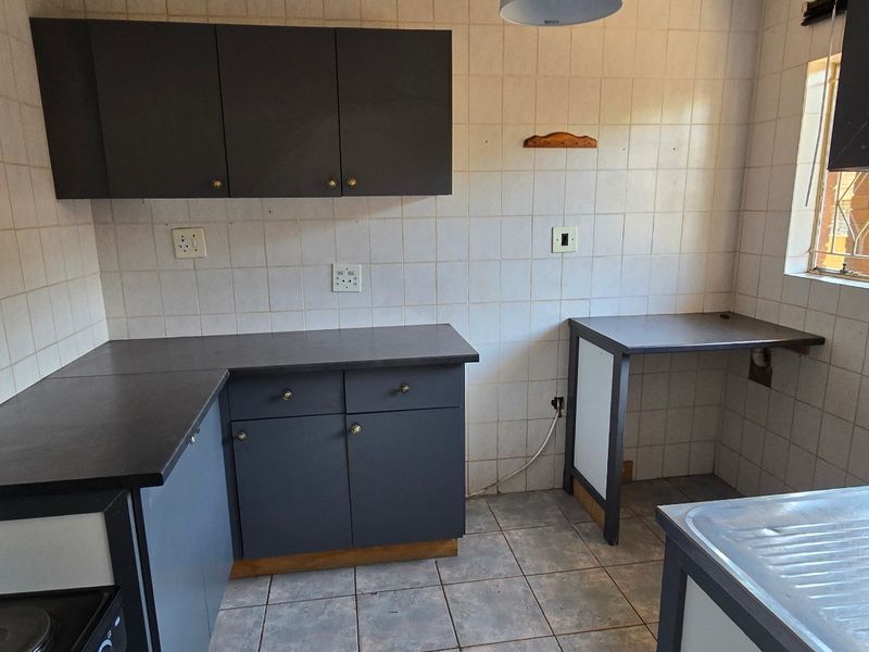 A functional, empty kitchen featuring dark cabinetry, tiled backsplash, and tiled flooring, offering a blank canvas for modern renovation and design updates.