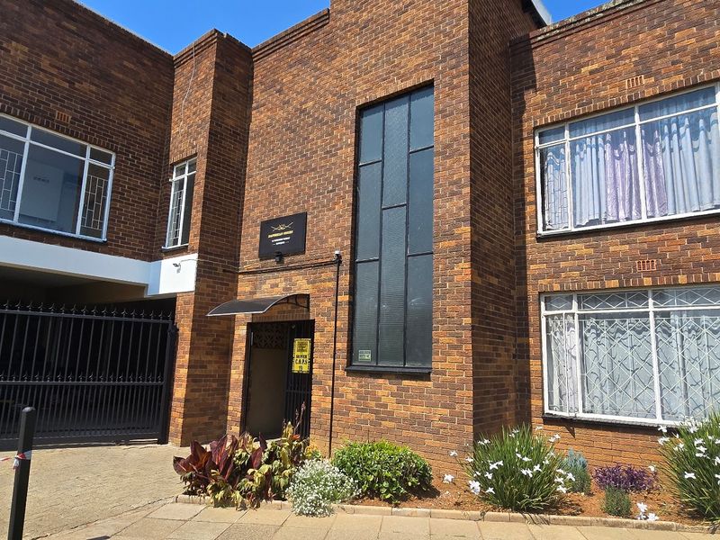 Front elevation of a multi-story apartment building featuring classic face brick construction, secure gated access, and metal-framed windows with security bars.