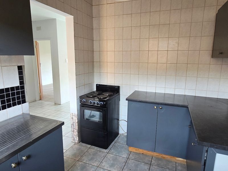 A functional kitchen featuring dark cabinetry, laminate countertops, a freestanding stove, and tiled surfaces, offering a blank canvas for modern updates.