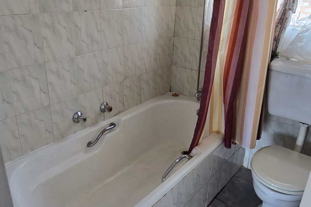 A functional bathroom featuring a bathtub with shower attachment and a standard toilet, finished with dated wall and floor tiling.