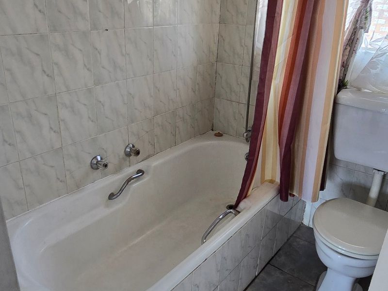 A functional bathroom featuring a bathtub with shower attachment and a standard toilet, finished with dated wall and floor tiling.