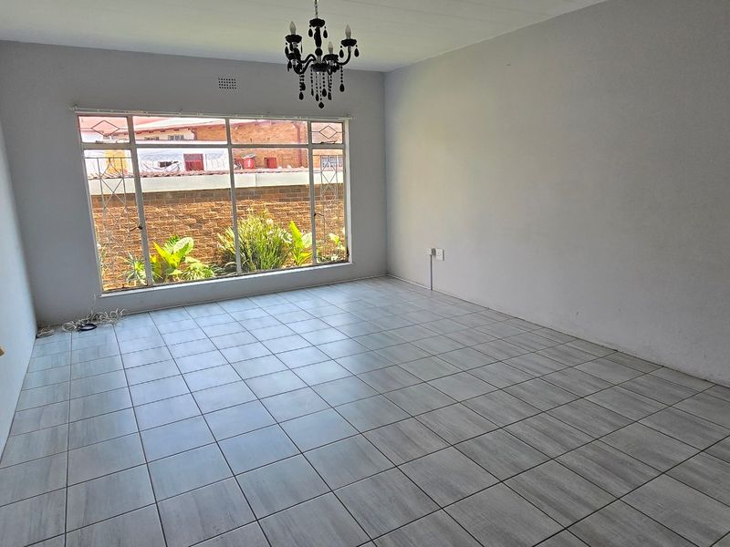 A bright, empty living room featuring neutral tiled flooring, a large window providing natural light, and a central ceiling light fixture.