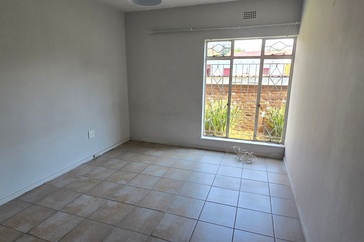 An empty bedroom featuring tiled flooring, a large window with security bars, and a curtain rail, providing a blank canvas for personalization.