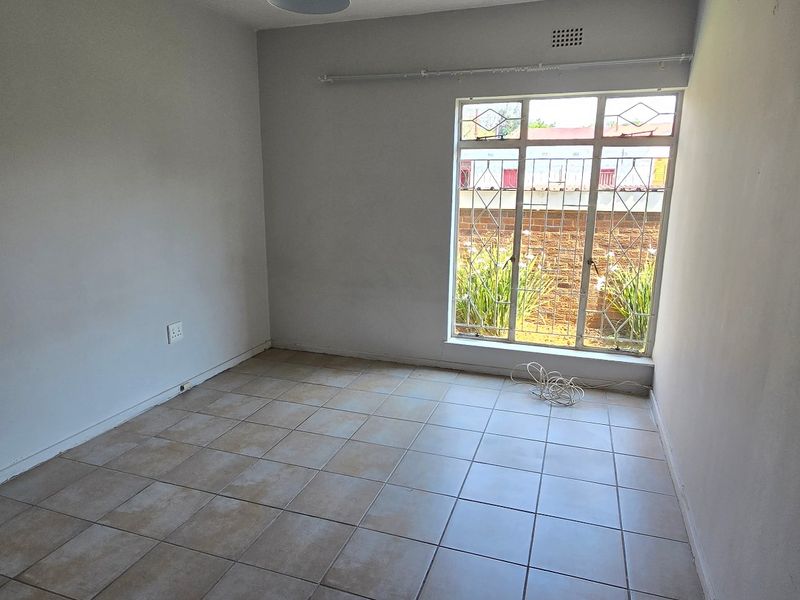An empty bedroom featuring tiled flooring, a large window with security bars, and a curtain rail, providing a blank canvas for personalization.
