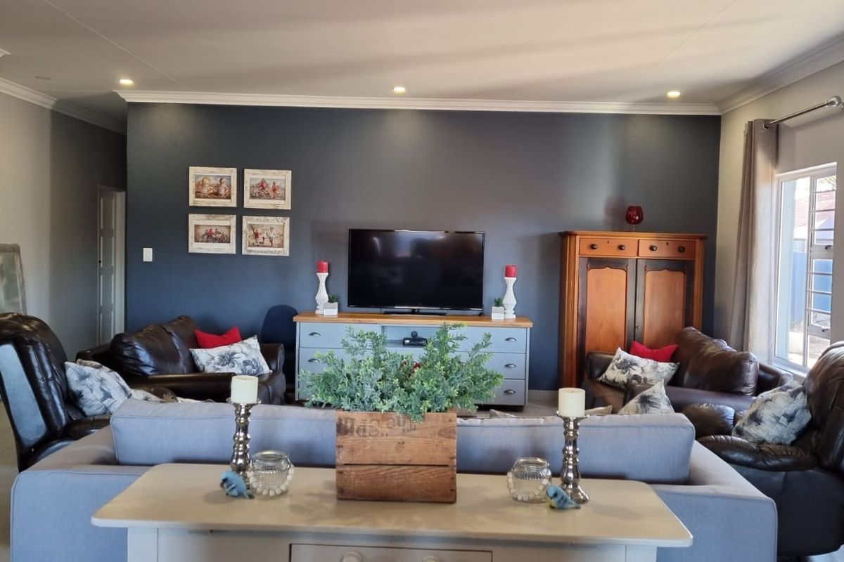 A spacious living room featuring a dark accent wall, recessed downlighting, and large windows, providing a comfortable and well-lit area for relaxation.