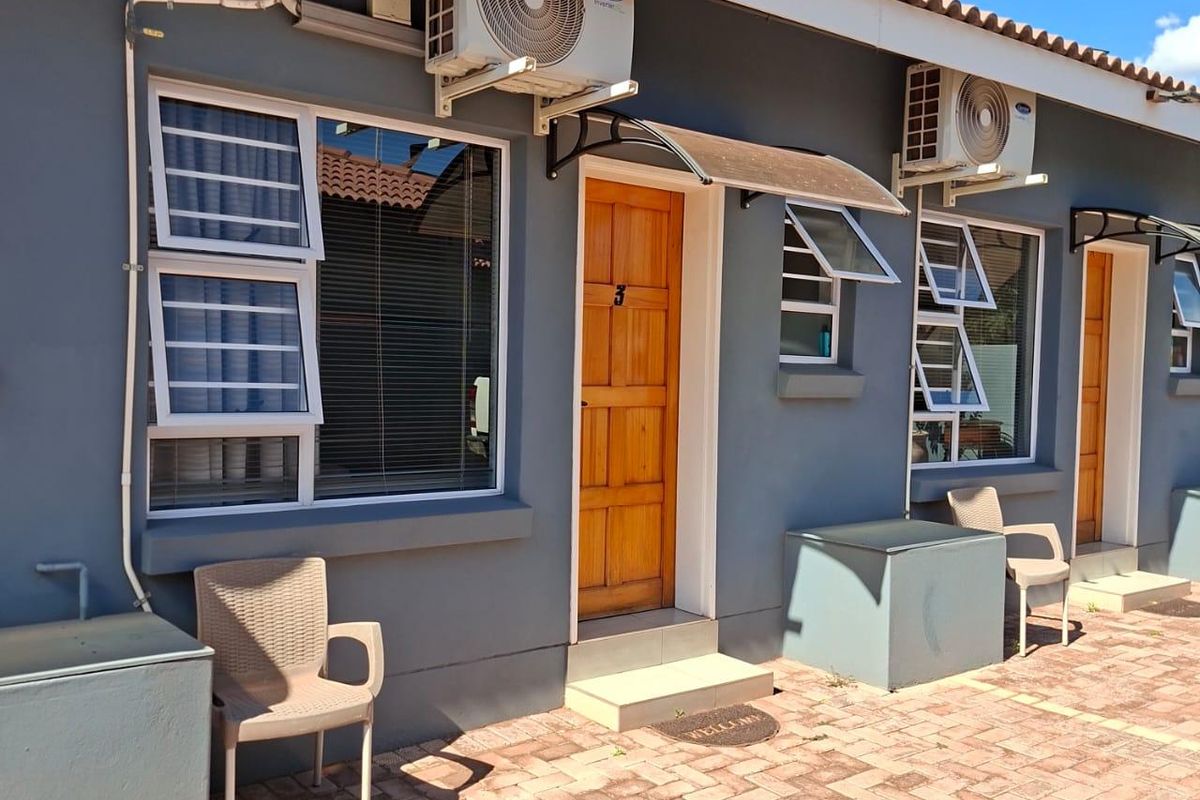 Exterior view of a residential unit featuring paved patio area, wooden entrance doors, aluminium windows, and wall-mounted air conditioning units.