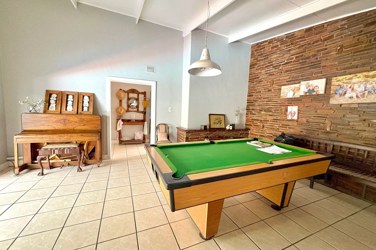 Spacious living area featuring a prominent exposed brick wall, vaulted ceilings with exposed beams, and neutral ceramic floor tiling.