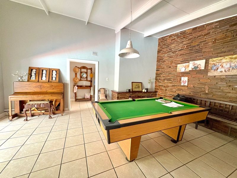 Spacious living area featuring a prominent exposed brick wall, vaulted ceilings with exposed beams, and neutral ceramic floor tiling.