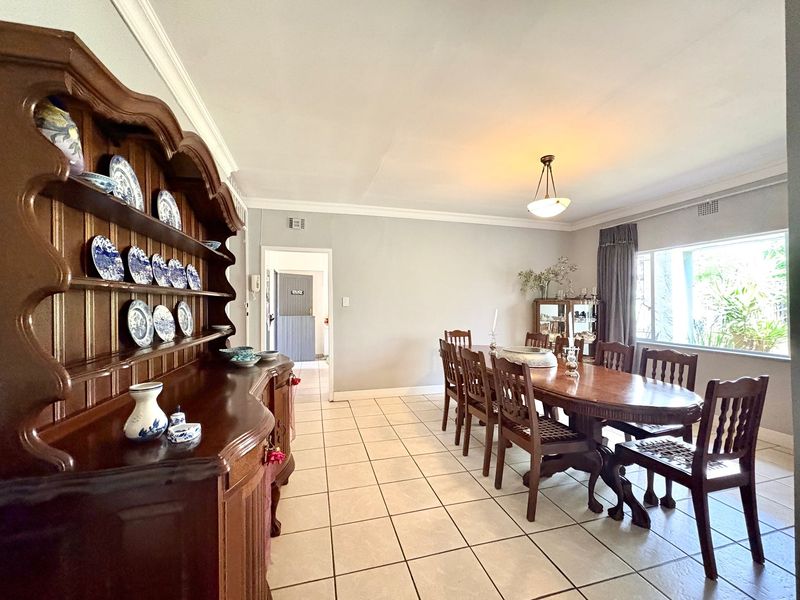 A spacious dining room featuring neutral wall tones, ceramic tiled flooring, and a large window providing natural light.