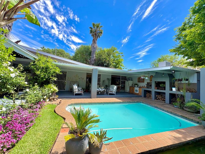 Outdoor entertainment area featuring a swimming pool, brick-paved surround, and a covered patio with a built-in braai facility.