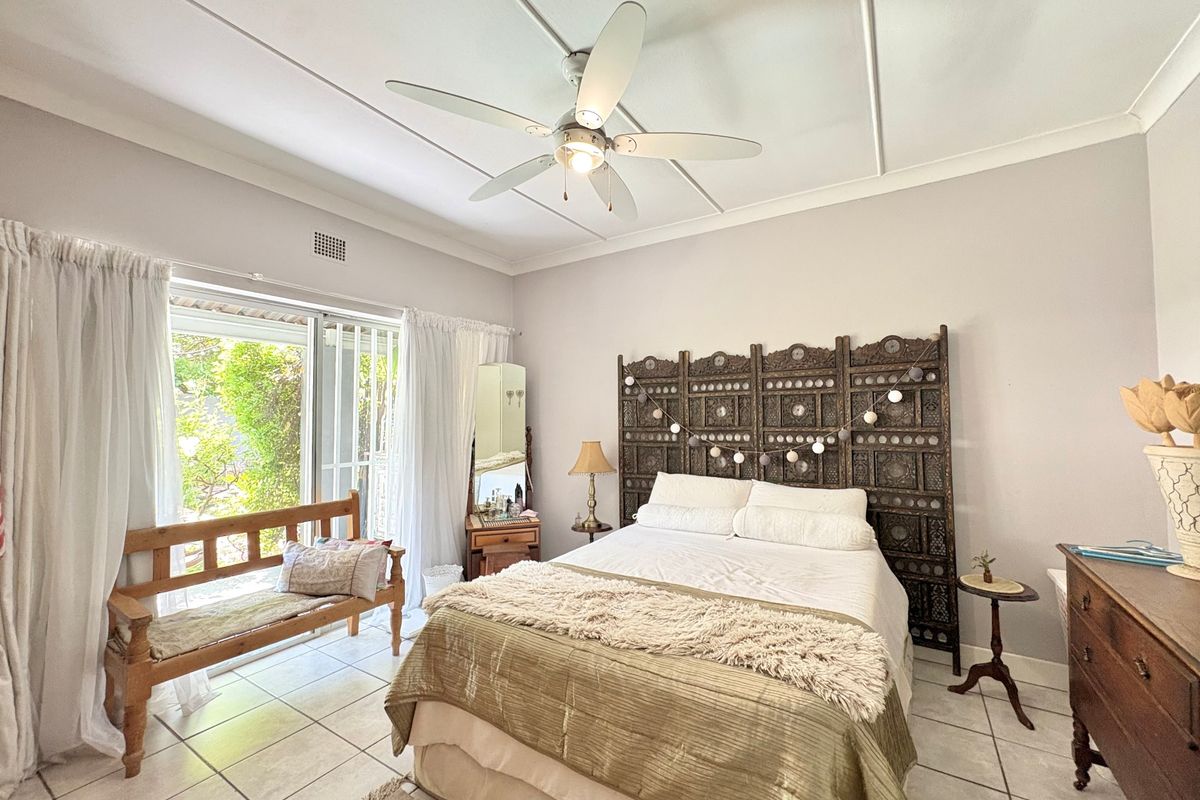 A bright bedroom featuring tiled flooring, a ceiling fan, and sliding glass doors providing access to the outdoor area.