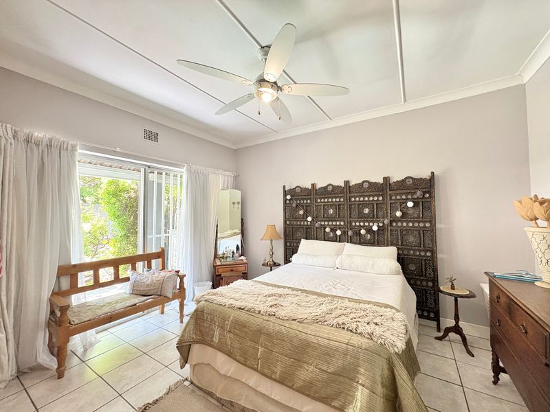 A bright bedroom featuring tiled flooring, a ceiling fan, and sliding glass doors providing access to the outdoor area.