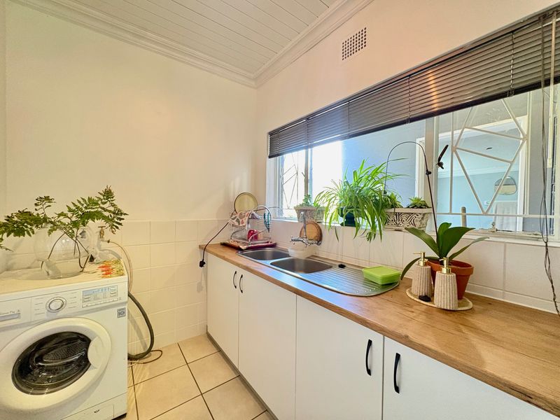 A functional laundry area featuring a stainless steel double sink, timber countertops, white cabinetry, and tiled splashbacks with natural light.