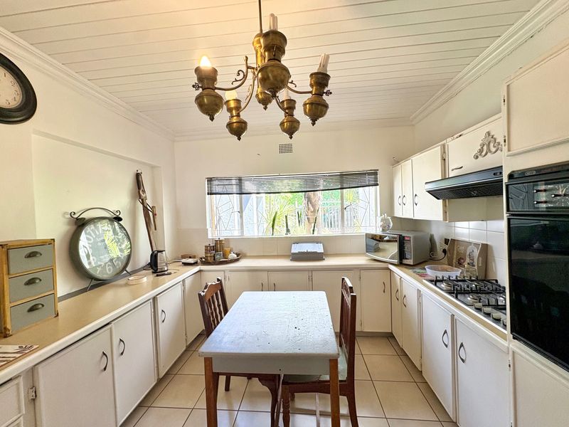 A functional kitchen featuring white built-in cabinetry, a gas hob, built-in oven, extractor fan, and tiled flooring under a classic tongue and groove ceiling.