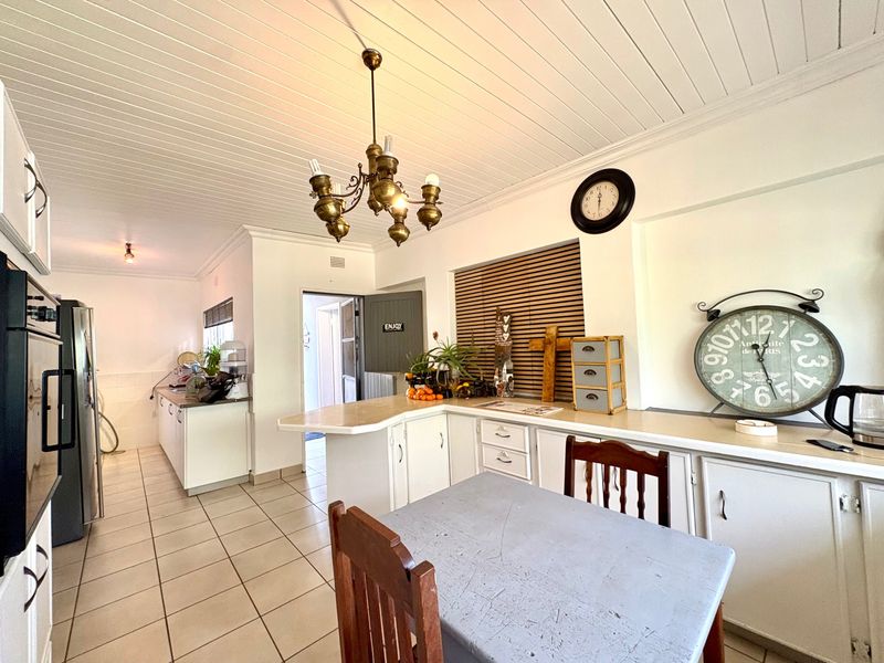A functional kitchen featuring white built-in cabinetry, laminate countertops, tiled flooring, and a distinctive tongue and groove ceiling with a central chandelier.