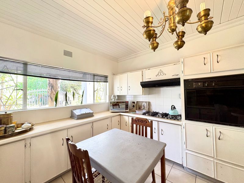 A functional kitchen featuring white built-in cabinetry, a gas hob, integrated oven, tiled backsplash, and a classic tongue and groove ceiling.