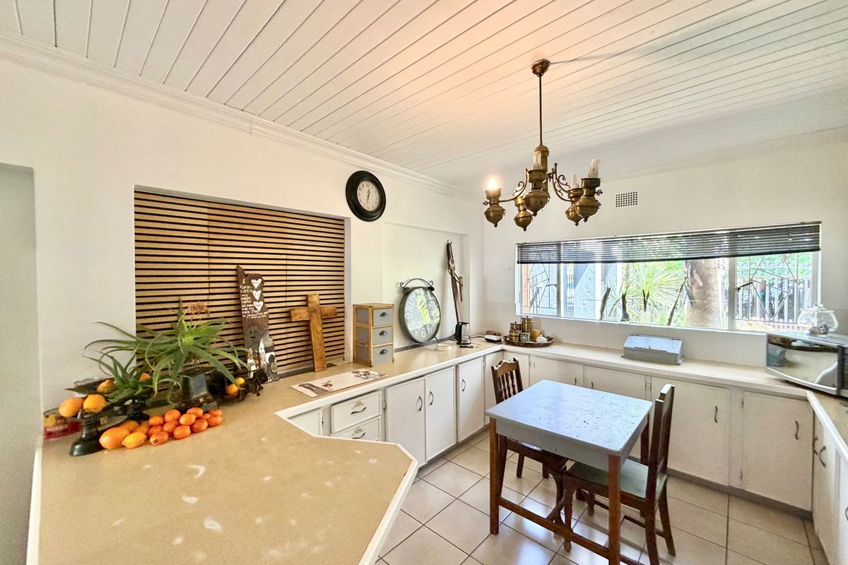 A functional kitchen featuring white cabinetry, laminate countertops, tiled flooring, and a distinctive tongue and groove ceiling with a classic brass chandelier.
