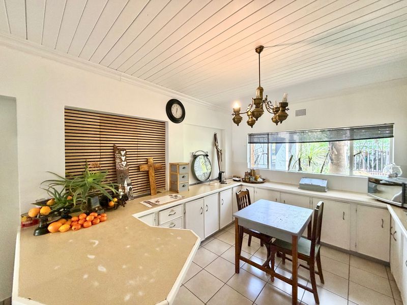 A functional kitchen featuring white cabinetry, laminate countertops, tiled flooring, and a distinctive tongue and groove ceiling with a classic brass chandelier.