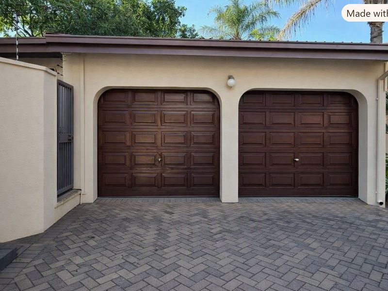 A well-maintained double garage featuring classic dark wood-finish doors and a neat herringbone-patterned paved driveway.