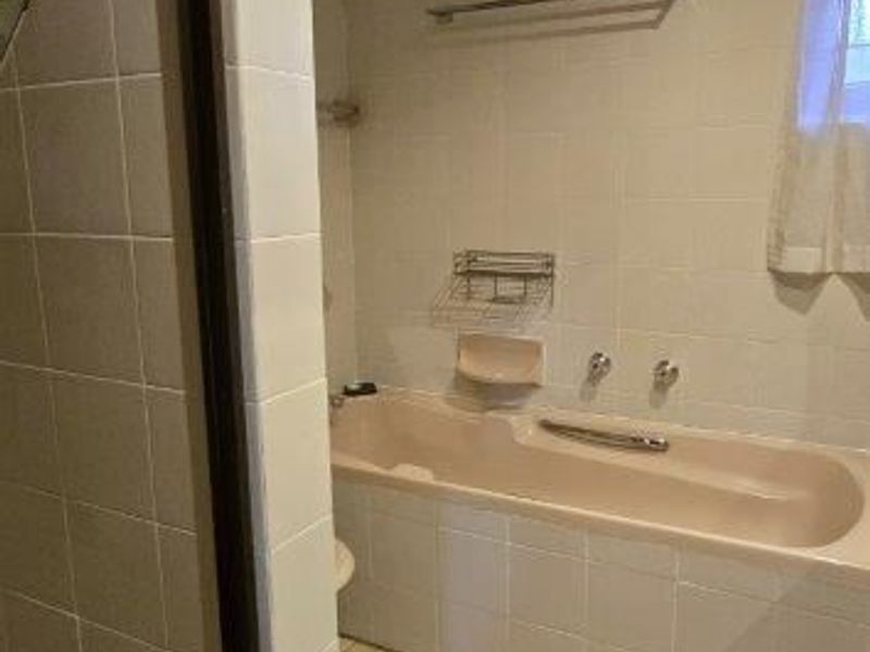 A dated bathroom featuring a built-in bathtub, separate shower enclosure, and tiled finishes throughout, offering potential for a modern renovation.