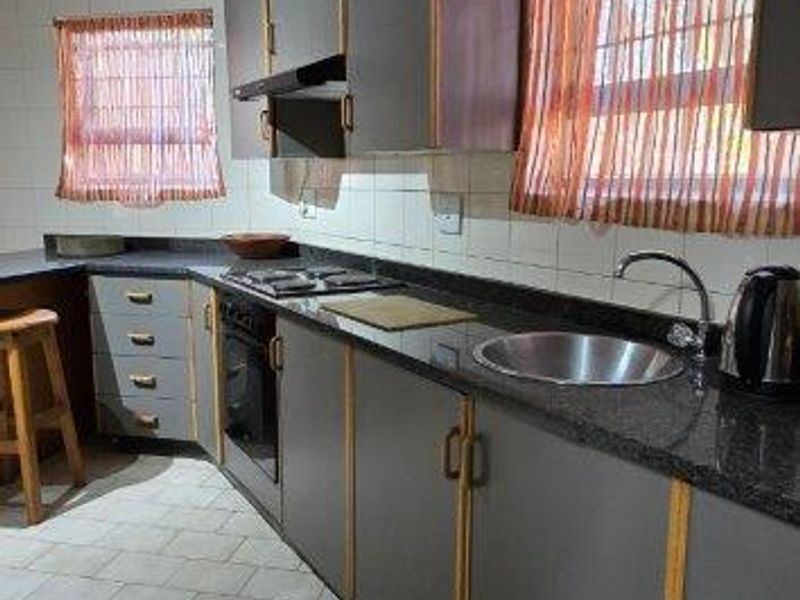 A functional kitchen featuring dark grey cabinetry, granite countertops, built-in oven, hob, and tiled flooring with a classic layout.
