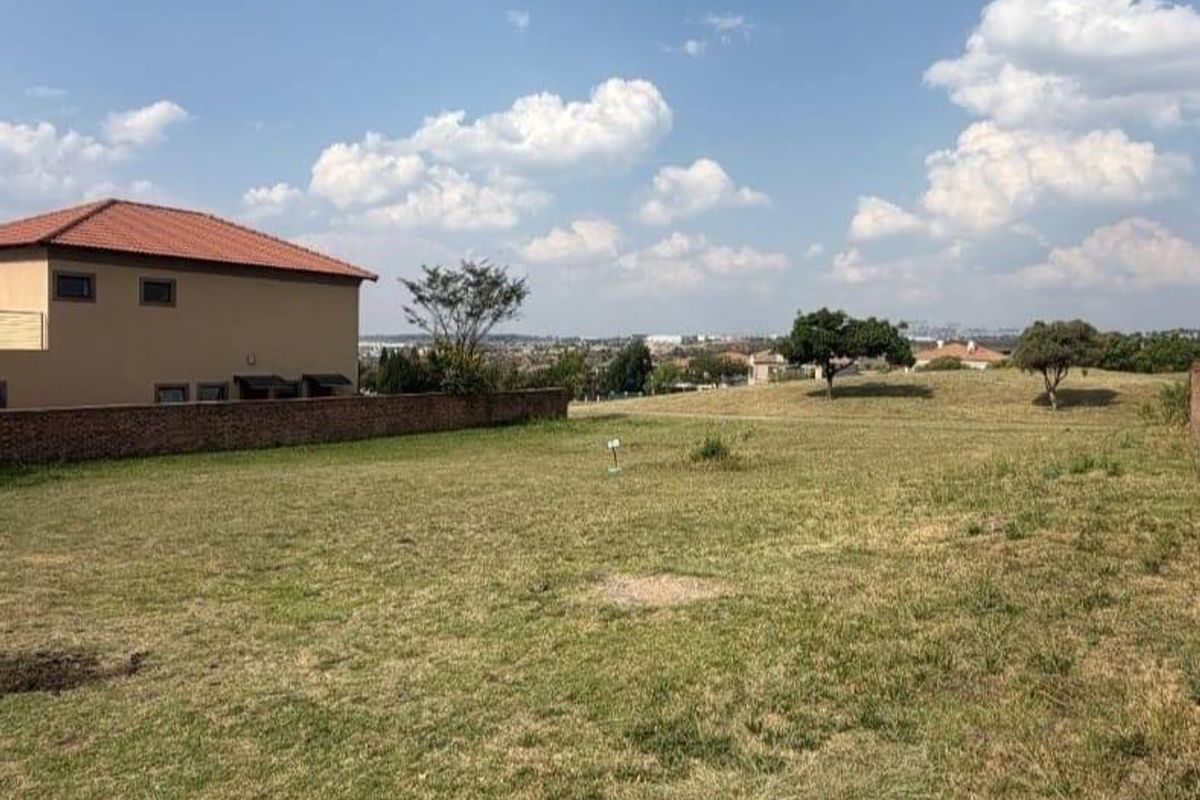 A vacant residential plot featuring a grass lawn and a boundary wall, offering an open view of the surrounding neighborhood.