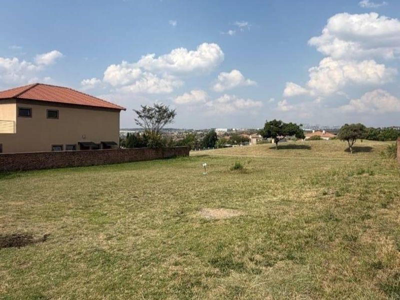 A vacant residential plot featuring a grass lawn and a boundary wall, offering an open view of the surrounding neighborhood.
