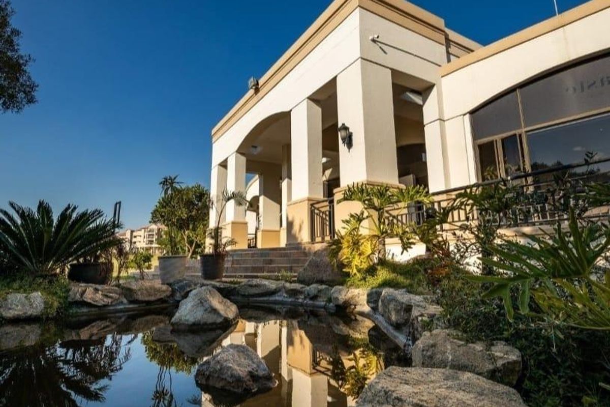 A well-maintained front exterior view featuring a decorative stone-lined pond and a covered patio area with architectural pillars.