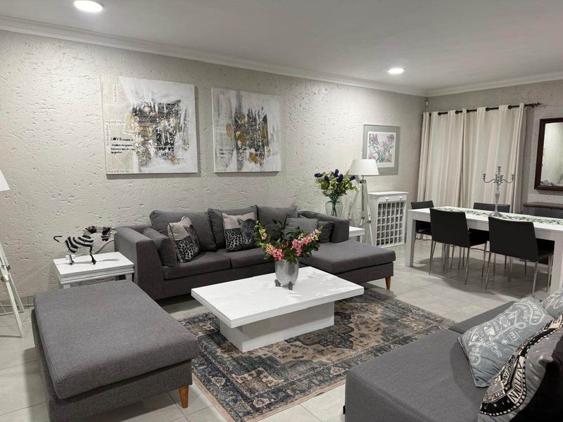 Spacious open-plan living and dining area featuring neutral textured walls, tiled flooring, and recessed downlighting, creating a bright and functional living space.