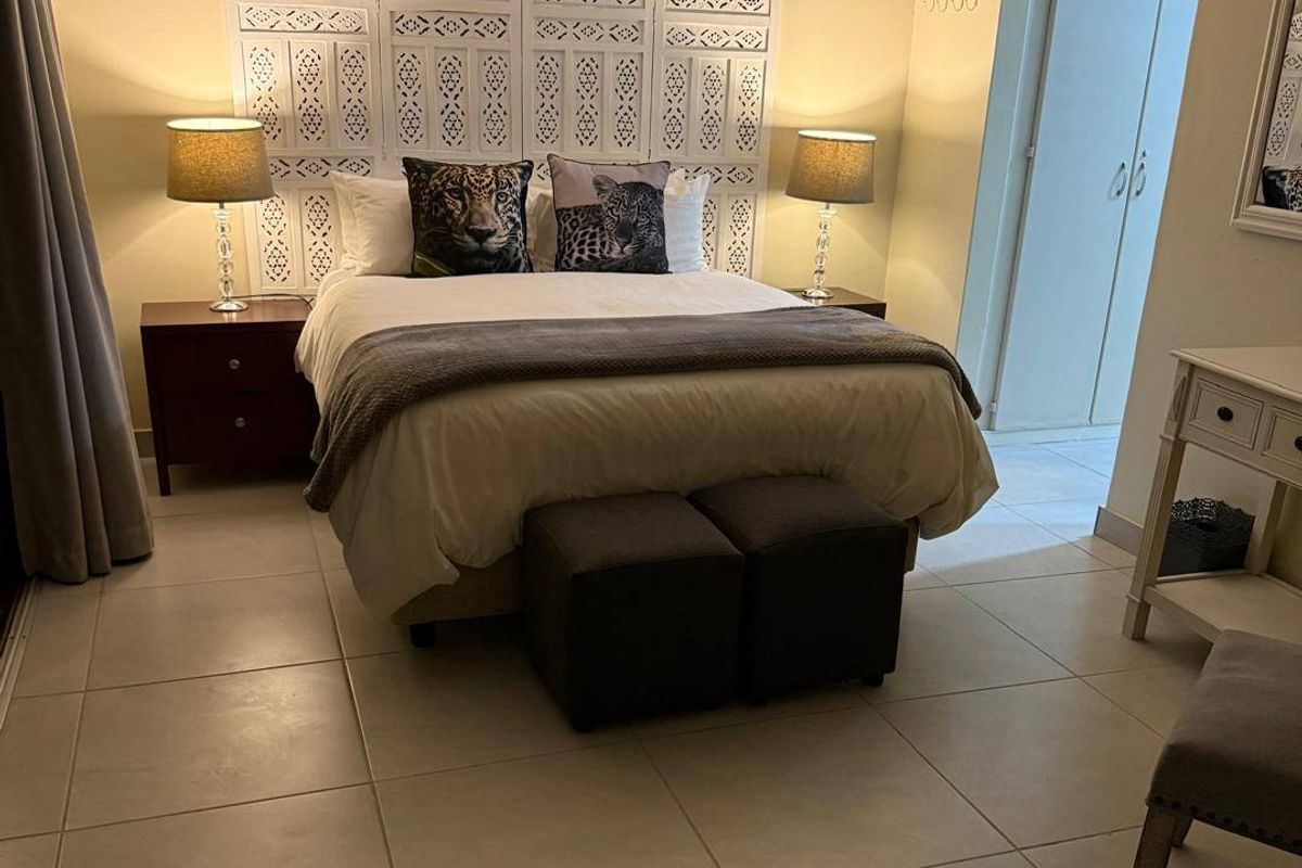 A well-maintained bedroom featuring neutral tiled flooring, cove ceiling detailing, and access to an adjoining space with built-in storage.